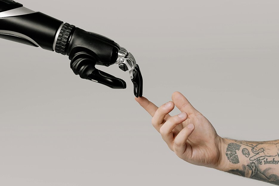 eine Roboterhand und eine menschliche Hand stellen die Hände von Gott und Adam aus dem Gemälde "die Erschaffung Adams" von Michelangelo nach