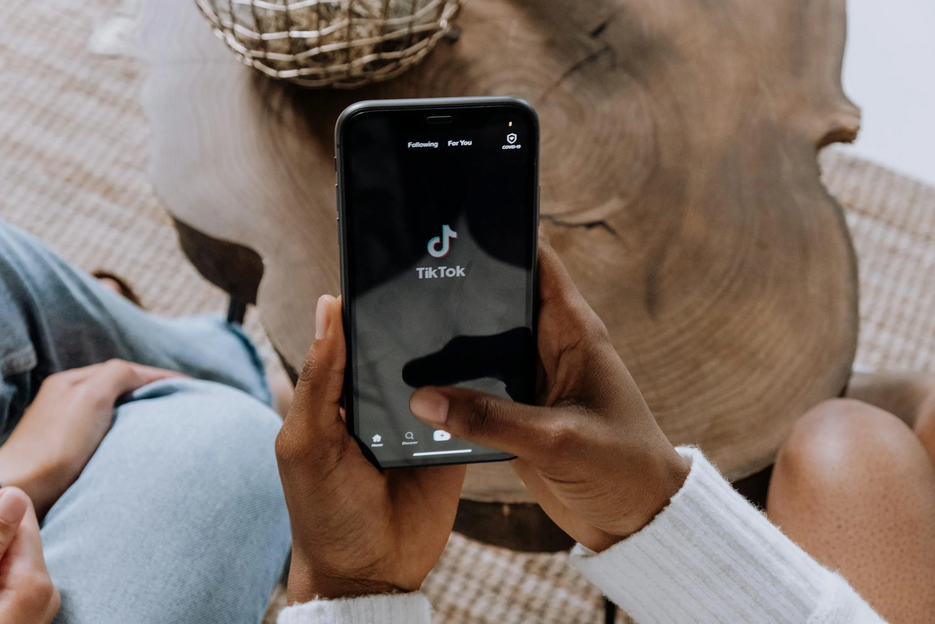 POV einer Person, die ein Smartphone in der Hand hält. Auf dem Bildschirm ist das Tiktok-Logo zu sehen