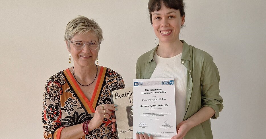 Julia Winkler (rechts im Bild) erhält eine Urkunde von Dekanin Prof. Andrea Kübler (links im Bild). Beide lächeln freundlich in die Kamera