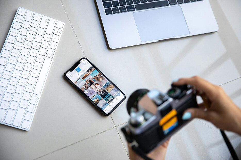 Eine Kamera fotografiert digitale Geräte (Smartphone, Laptop, Tastatur)